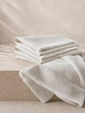 A stack of folded off-white linen napkins with frayed edges, draped over a beige stone block against a matching neutral background.