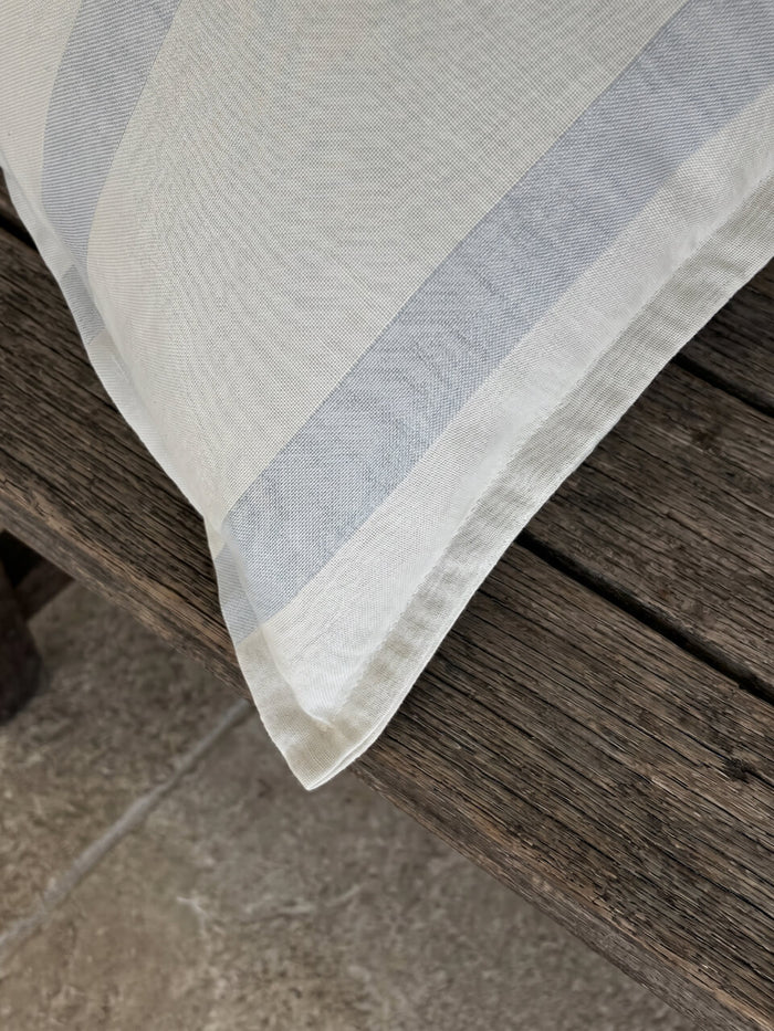 Close-up detail of a luxury blue fog striped cotton linen cushion cover with tailored edging, styled on a rustic timber surface to showcase its soft woven texture and refined craftsmanship.