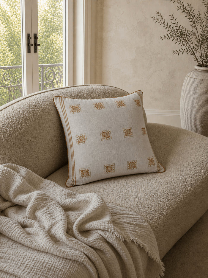 Luxury cream and caramel patterned cotton cushion cover with woven geometric detailing, styled on a textured boucle armchair in a warm contemporary interior.