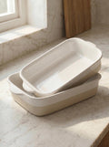 Set of two beige ceramic baking dishes on a marble countertop with natural light.