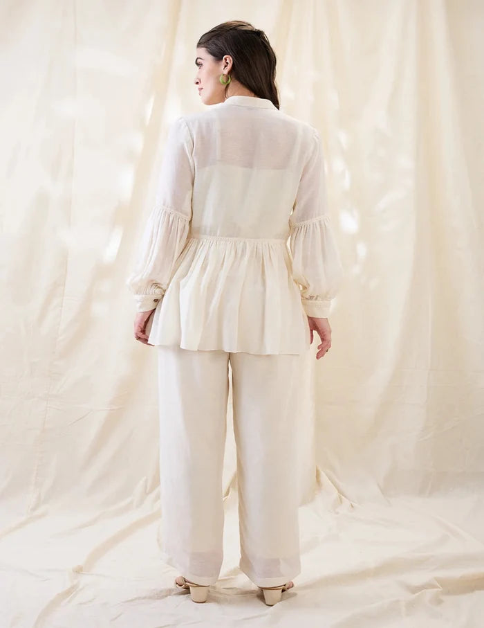 White Gulzaar Appliquéd Peplum Top with front tie-ups paired with straight linen pants, offering an elegant and refined contemporary silhouette.
