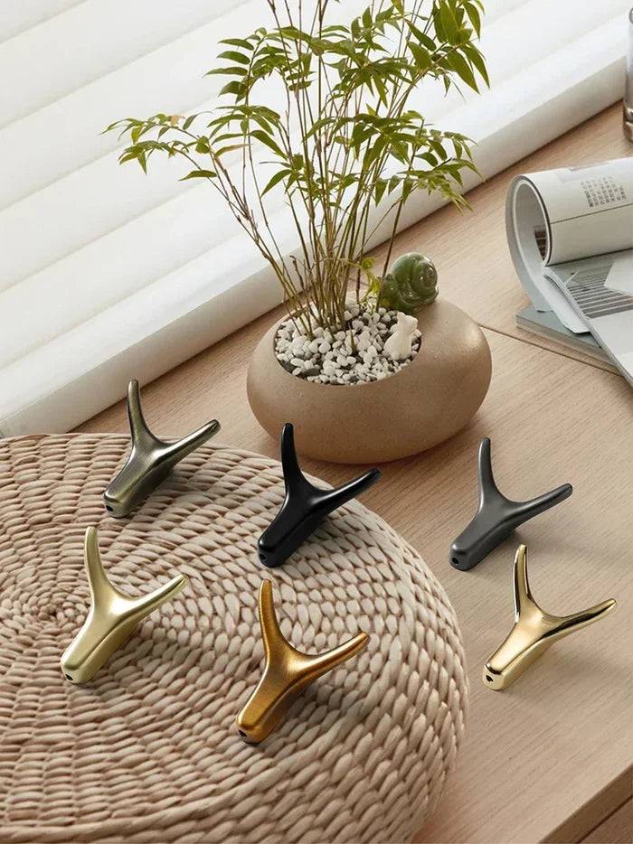Modern antler-shaped hooks in gold, black, and bronze on woven mat with potted plant