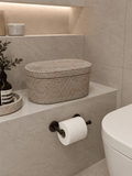 Bathroom setting with a Jarra rattan basket, toilet paper roll, and plant on a shelf.