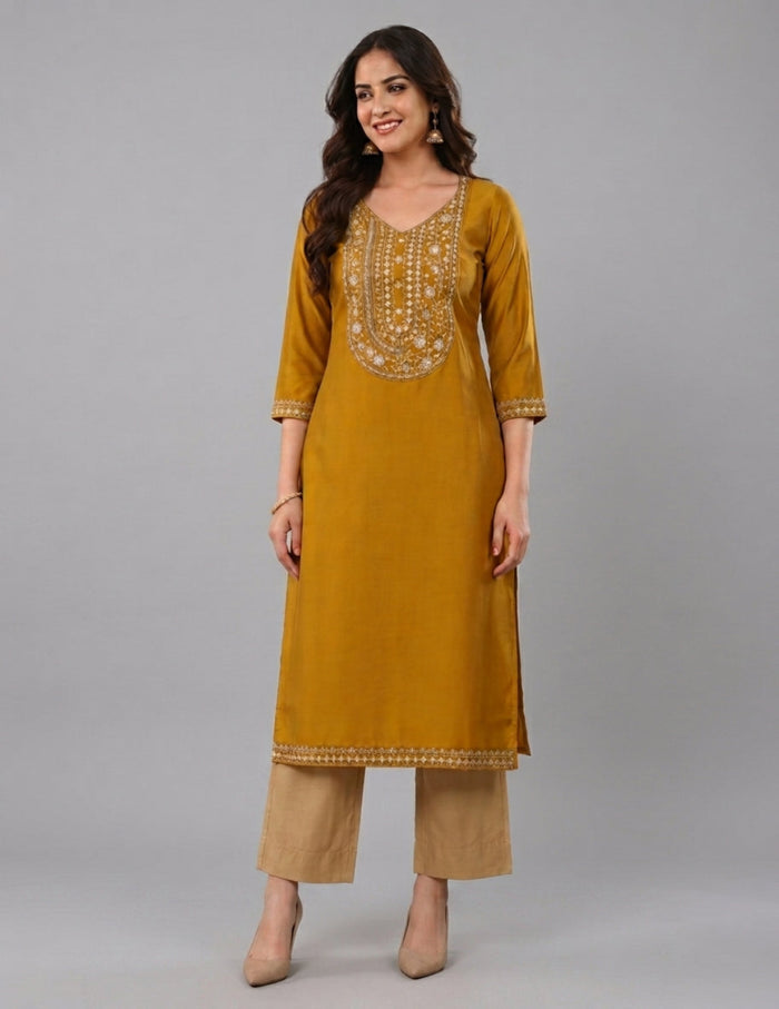 A woman modeling a mustard yellow kurta with gold embroidery on the chest and cuffs, paired with beige pants, against a solid gray studio background.