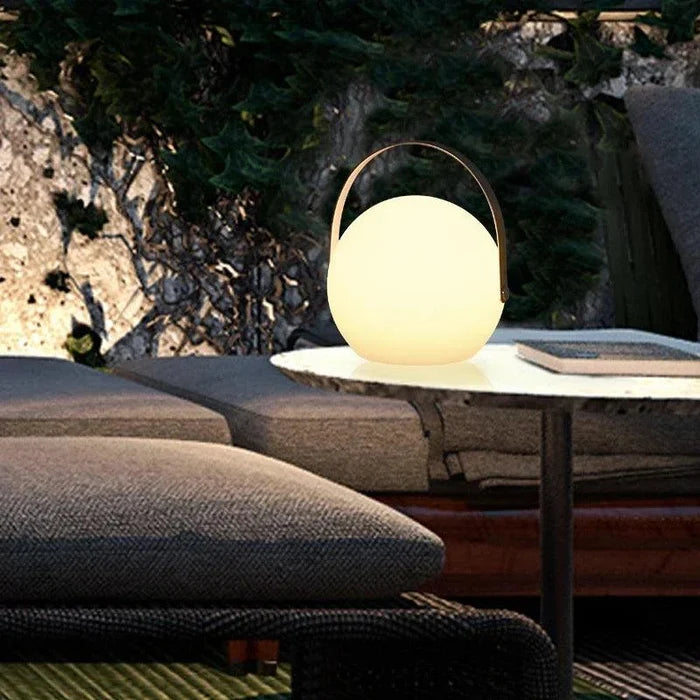 Glowing spherical lantern with handle on outdoor table, enhancing cozy patio ambiance