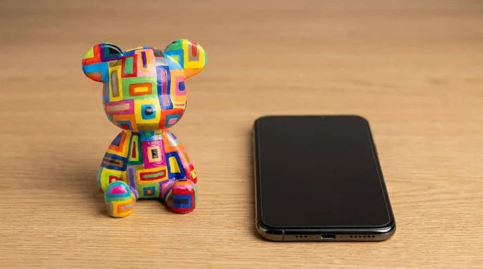 Colorful geometric bear figurine beside smartphone on wooden surface