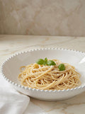 White bowl of spaghetti with green basil leaves on a marble surface