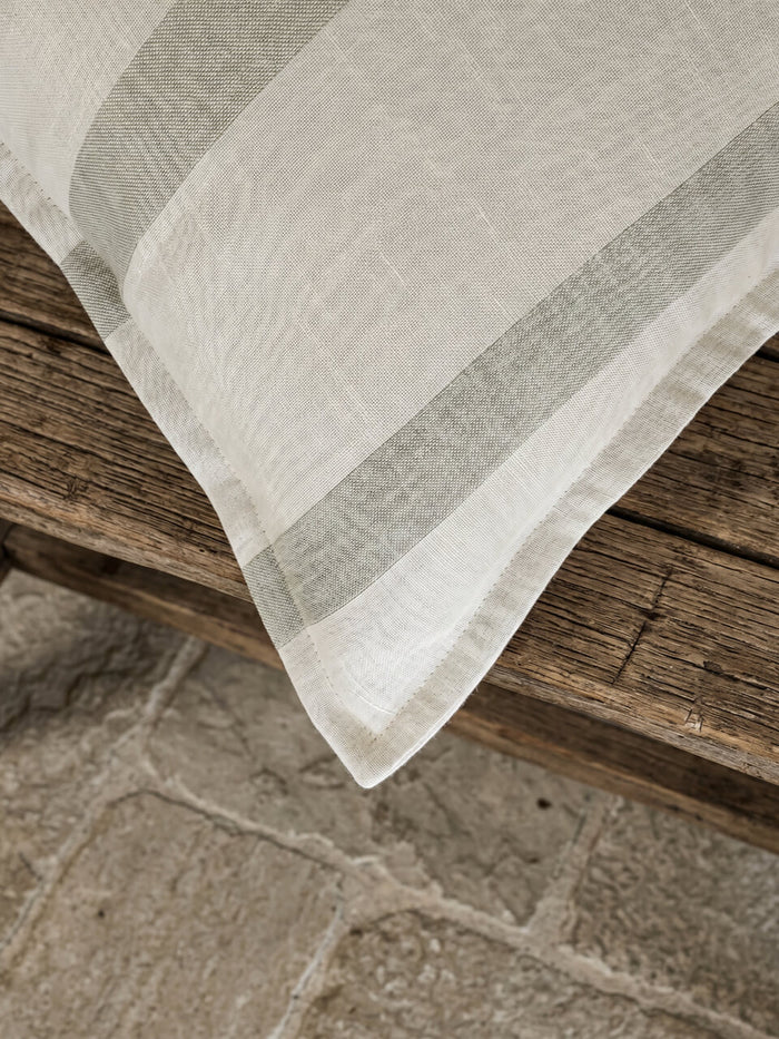 Close-up detail of a luxury sage green striped cotton linen cushion cover featuring soft woven texture and tailored edging, styled on rustic timber for a relaxed contemporary aesthetic.