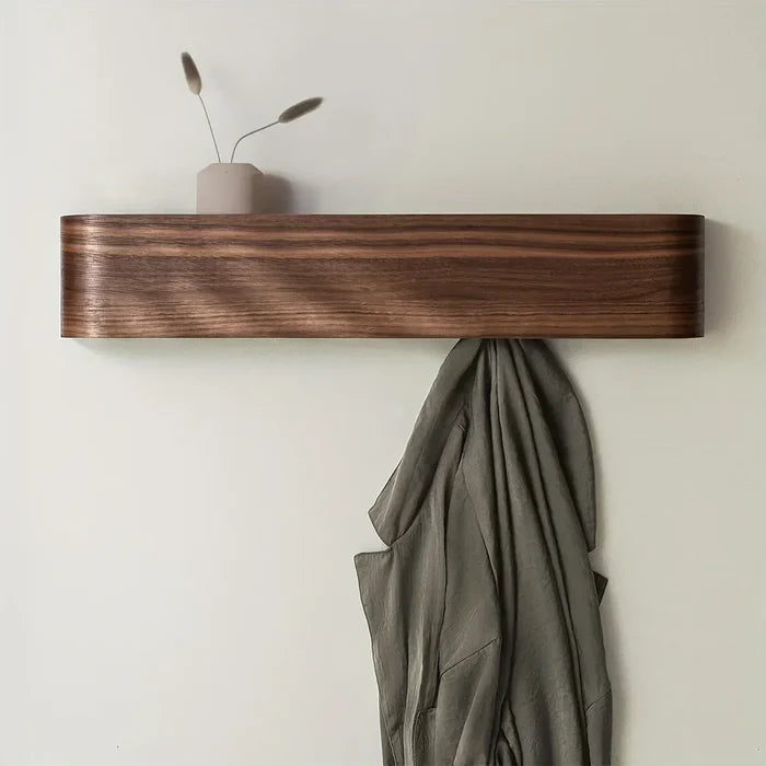 Wooden shelf on a white wall with a green garment and decorative vase.