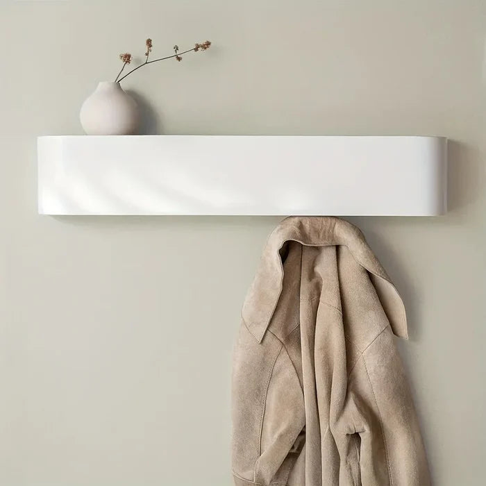 White wall-mounted shelf with a beige coat and a vase with branches on a light green wall.